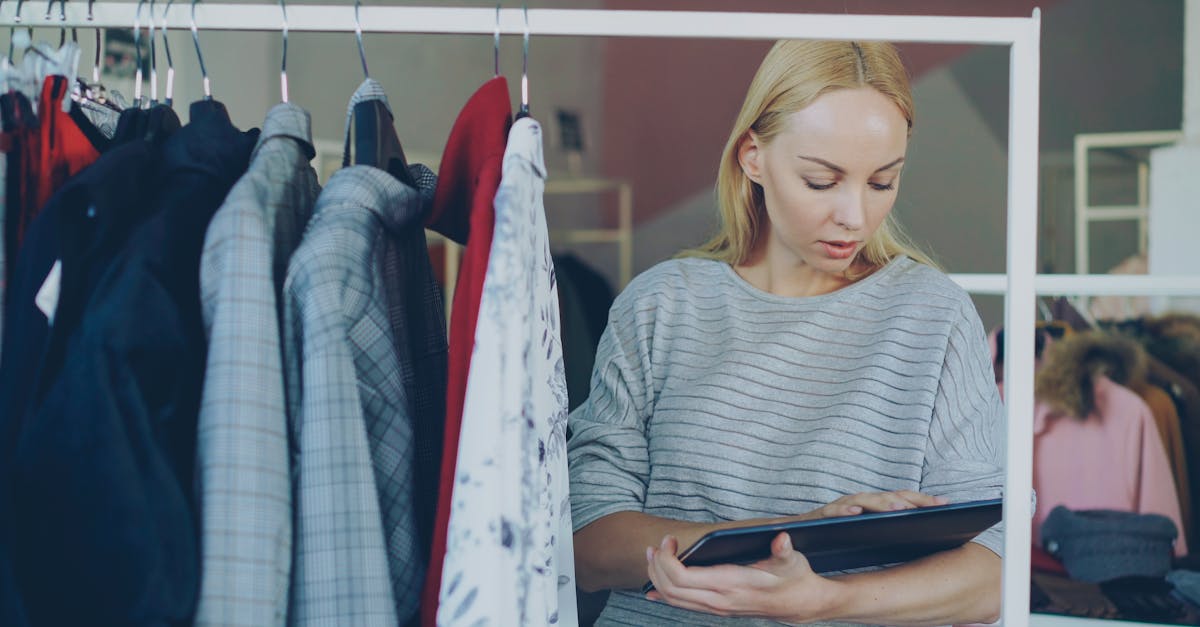 Vrouwelijke medewerkster controleert de voorraad in een kledingwinkel met behulp van een tablet.