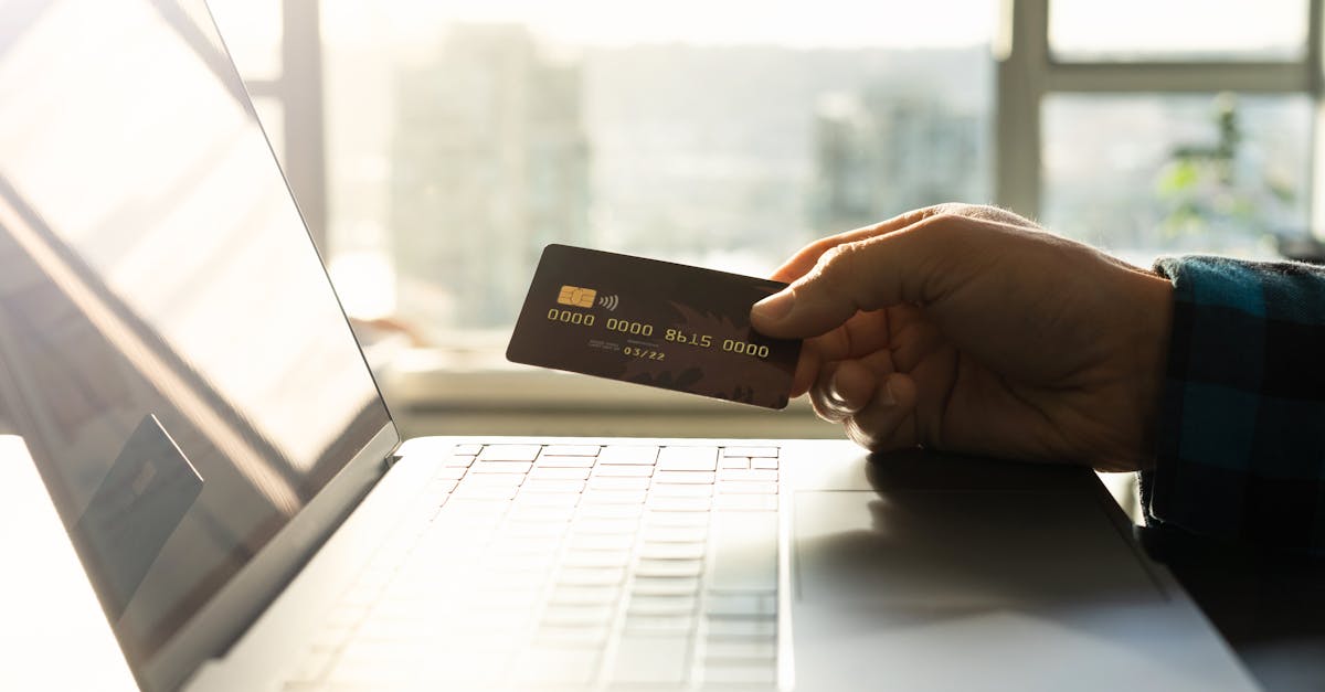 Een hand met een creditcard voor een laptop, symbool voor online winkelen en digitale betaling.